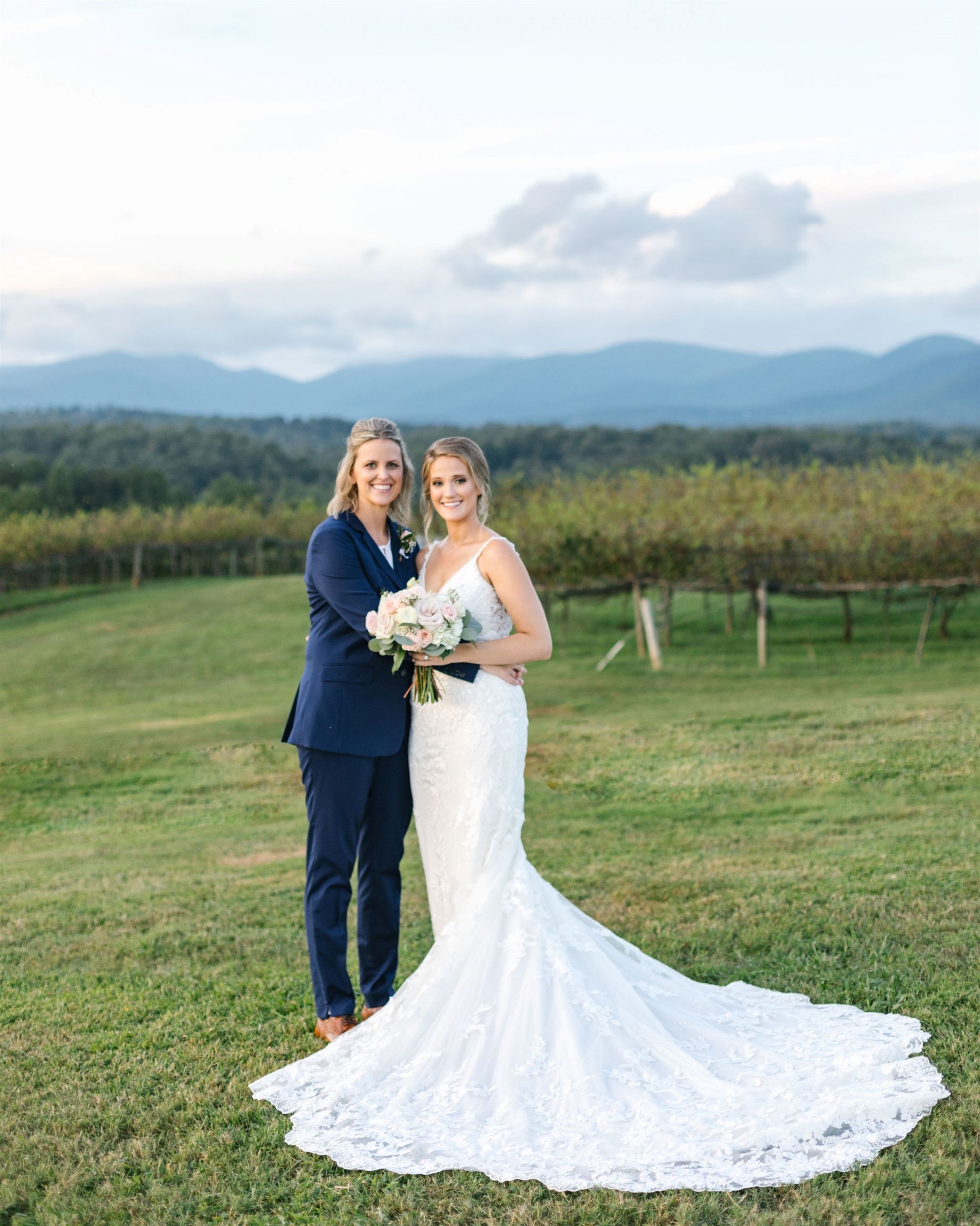 Two brides standing together in vineyard on wedding day