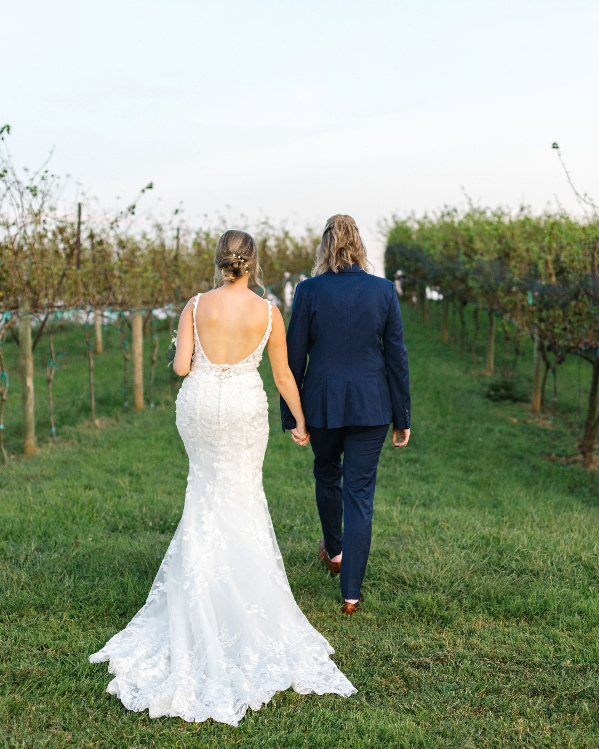 Two brides holding hands at their vineyard wedding